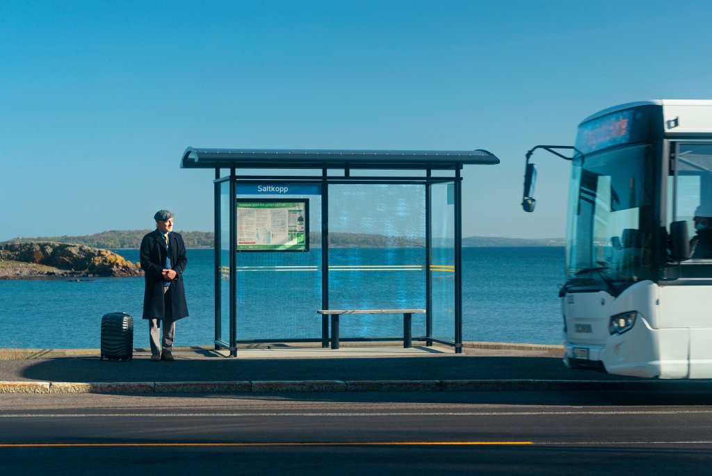 En mann står på en bussholdeplass og venter på bussen som kommer